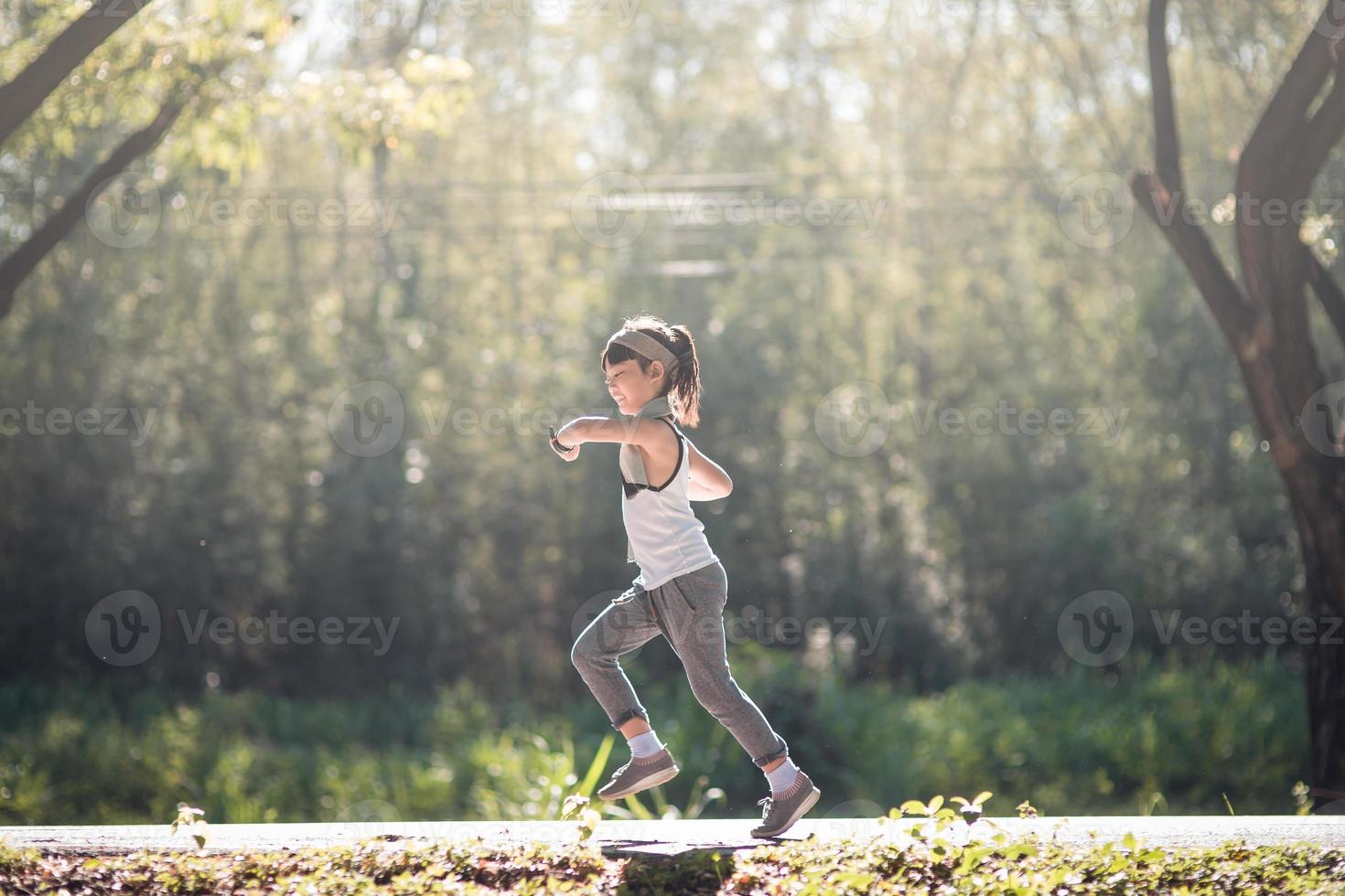 niña feliz corriendo en el parque en verano en la naturaleza. llamarada cálida de la luz del sol. el pequeño asiático corre en un parque. deportes al aire libre y fitness, ejercicio y aprendizaje de competencias para el desarrollo de los niños. foto