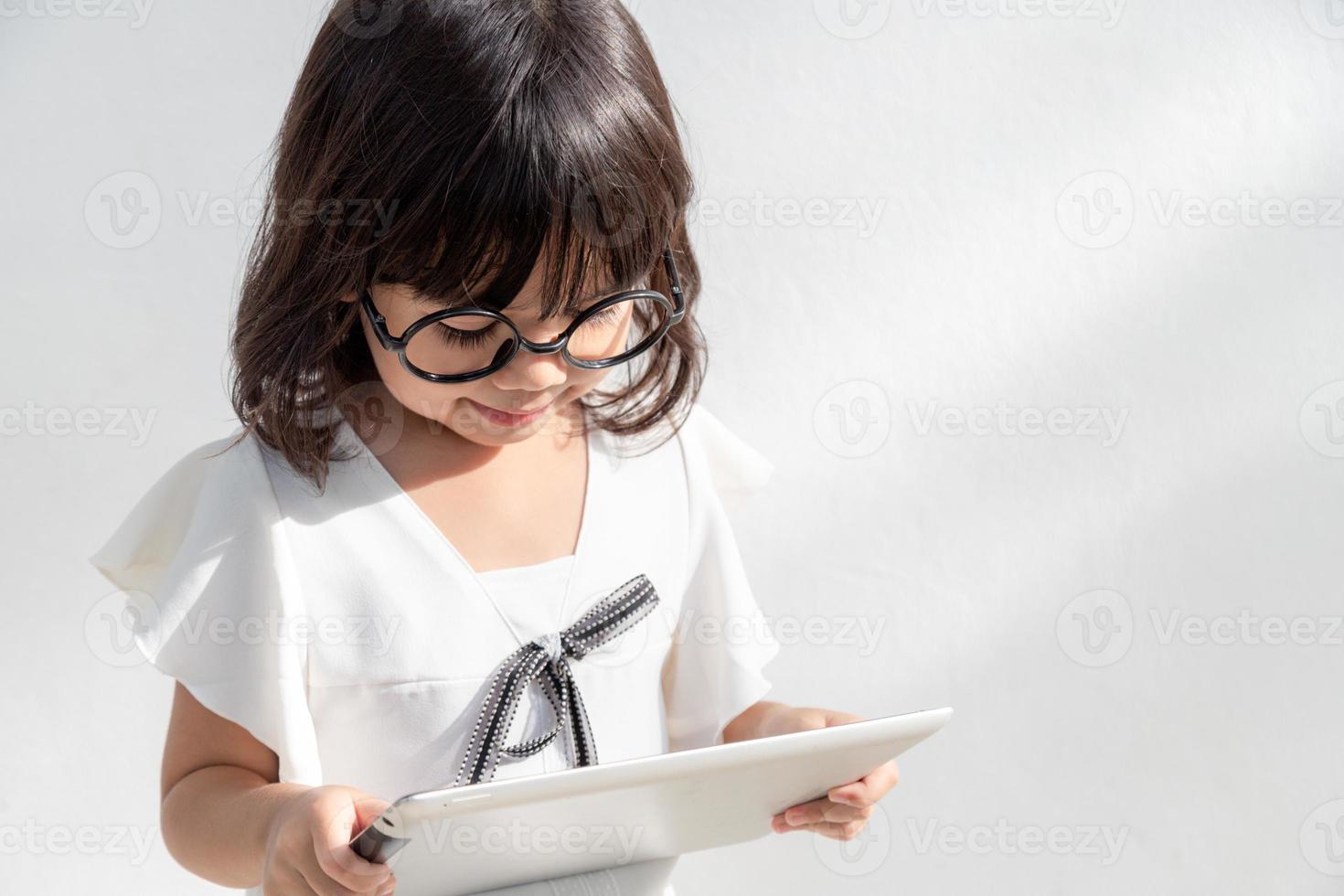 A little girl is concentrated on the tablet, look at the tablet, technology concept for children, profile view, isolated on white background, copy space photo