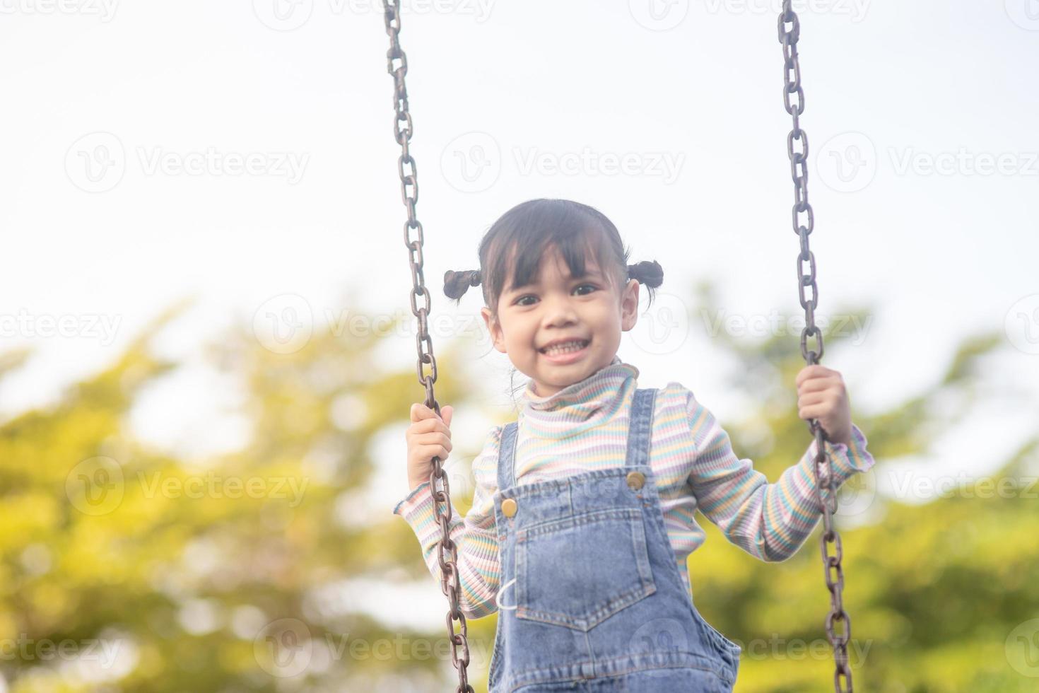 niña asiática feliz jugando al columpio al aire libre en el parque foto