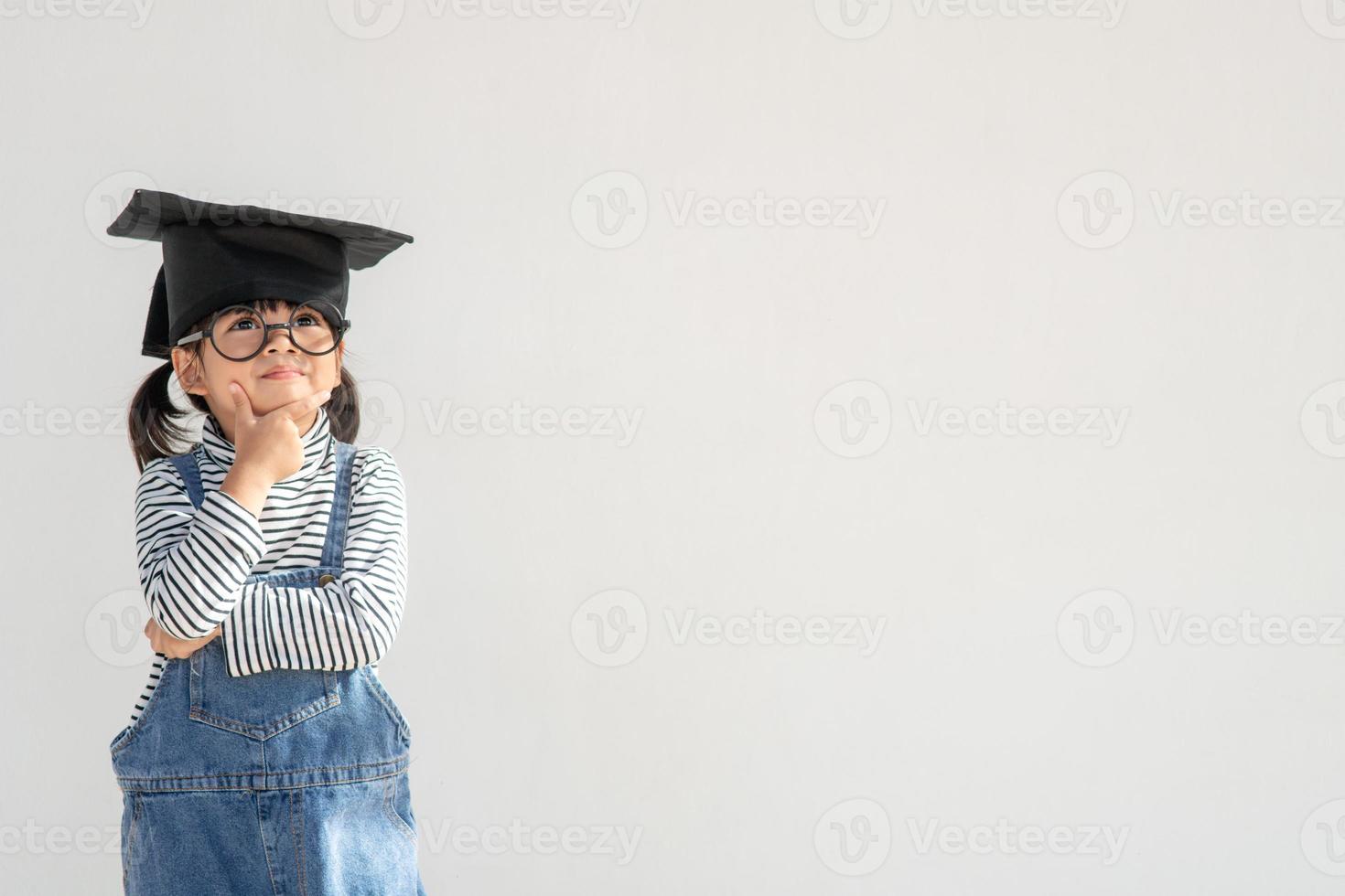 Happy Asian school kid graduate thinking with graduation cap photo