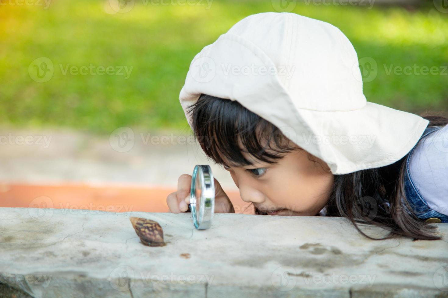 Happy kid girl exploring nature with a magnifying glass and a snail. He having fun in the garden. The concept of the kid is ready to go to school. photo