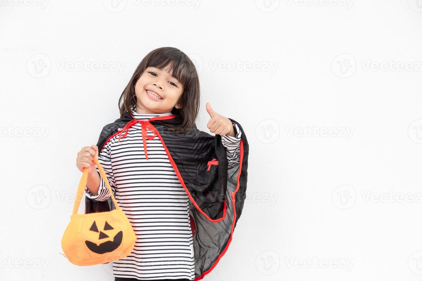 divertido concepto de niño de halloween, niña linda con disfraz de fantasma de halloween aterrador que sostiene un fantasma de calabaza naranja en la mano, sobre fondo blanco foto