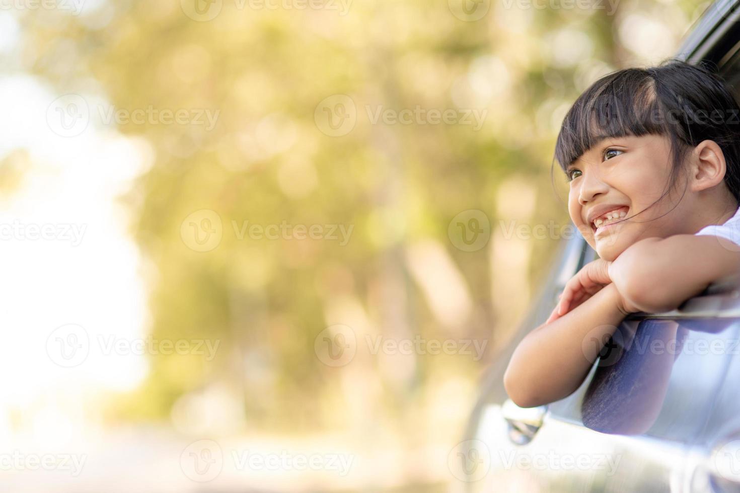 Cute asian little child girl having fun to travel by car and looking out from ar window in cthe countryside photo