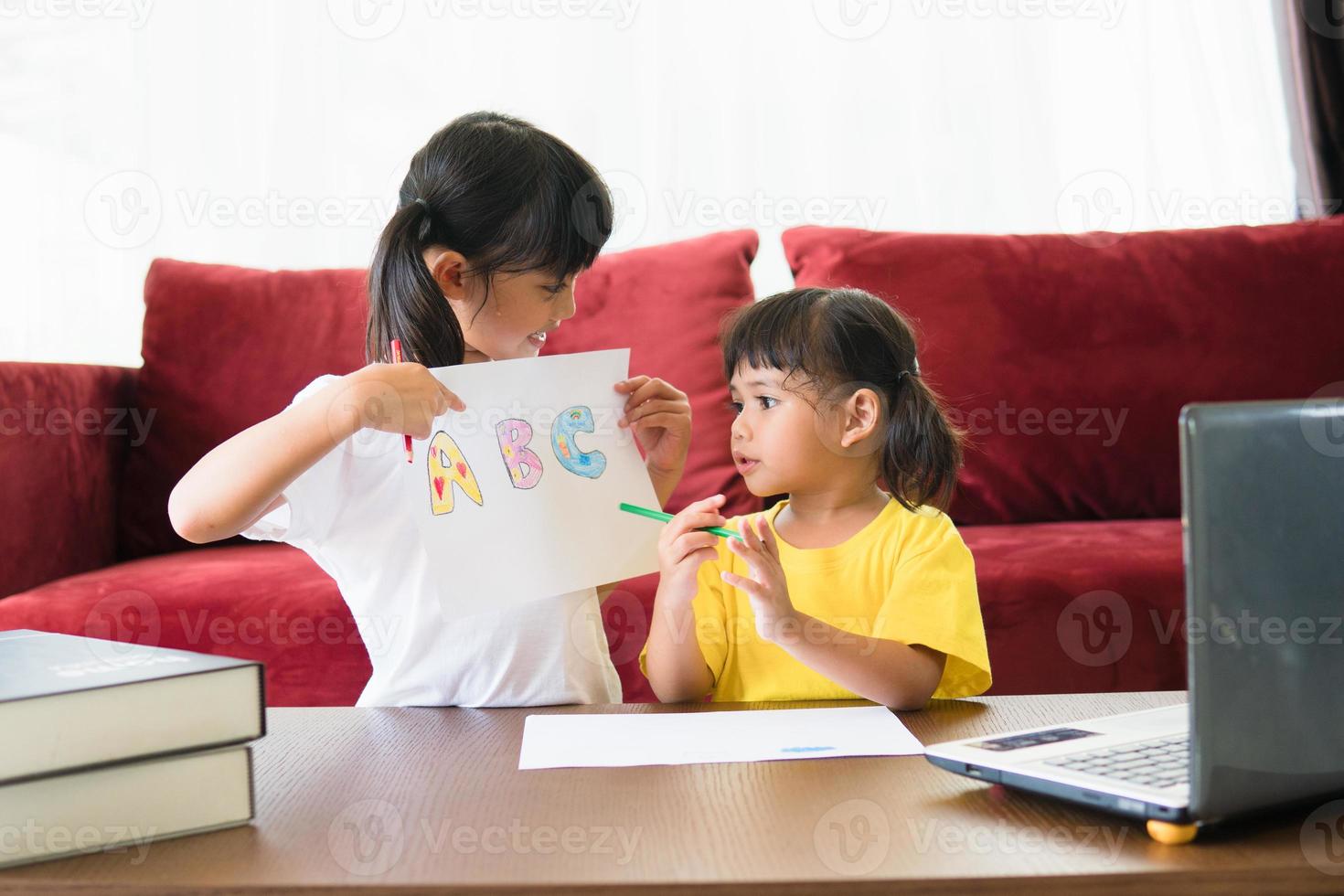 Two asian child girl students study online with teacher by video call together. Siblings are homeschooling with computer laptop during quarantine due to Covid 19 pandemic. photo