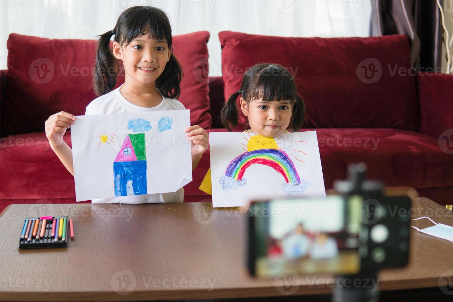 Two asian child girl students study online with teacher by video call together. Siblings are homeschooling with computer laptop during quarantine due to Covid 19 pandemic. photo