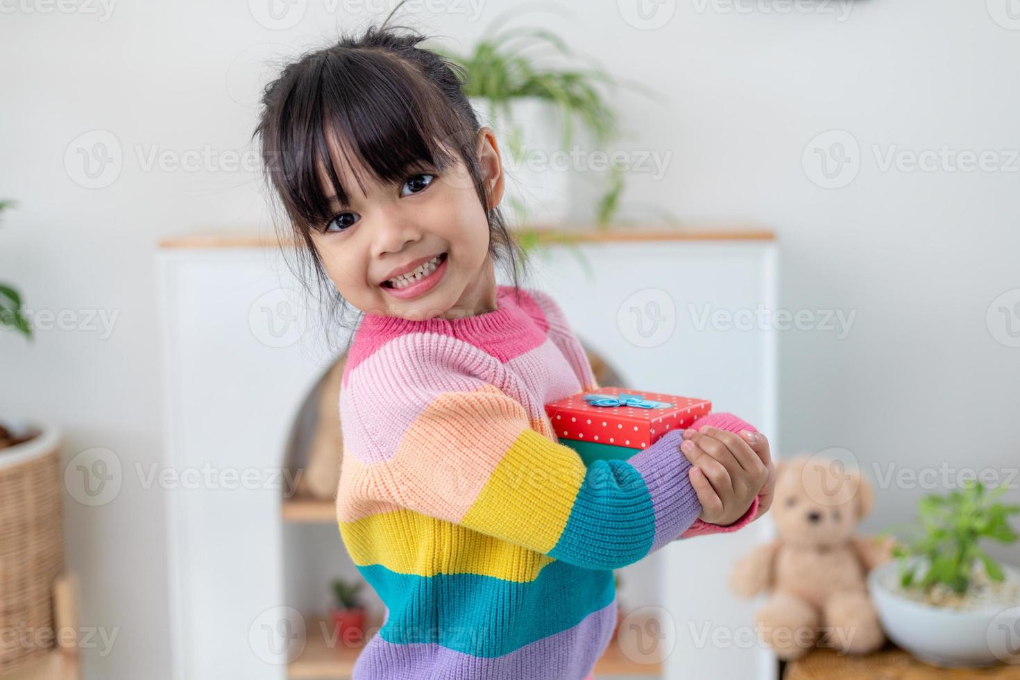 Little Asian girl smile and excited and holding red gift box in living room background. child holding gift box in Christmas and New year.Asian child girl smile and surprise. photo