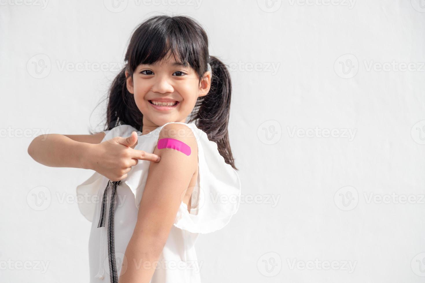 Asian little girl showing his arm after got vaccinated or inoculation, child immunization, covid delta vaccine concept photo