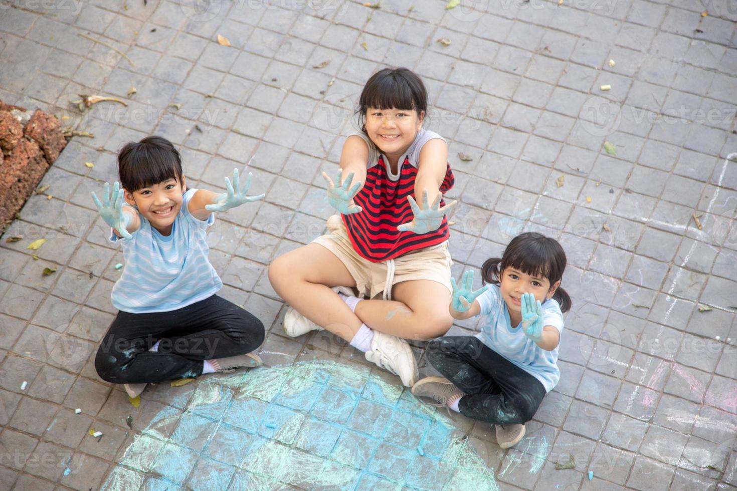 Asian children play outdoors. Child girl draws a planet globe with a map of the world colored chalk on the pavement, asphalt. Earth, peace day concert. photo