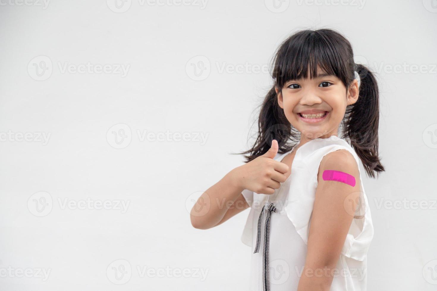 Asian little girl showing his arm after got vaccinated or inoculation, child immunization, covid delta vaccine concept photo