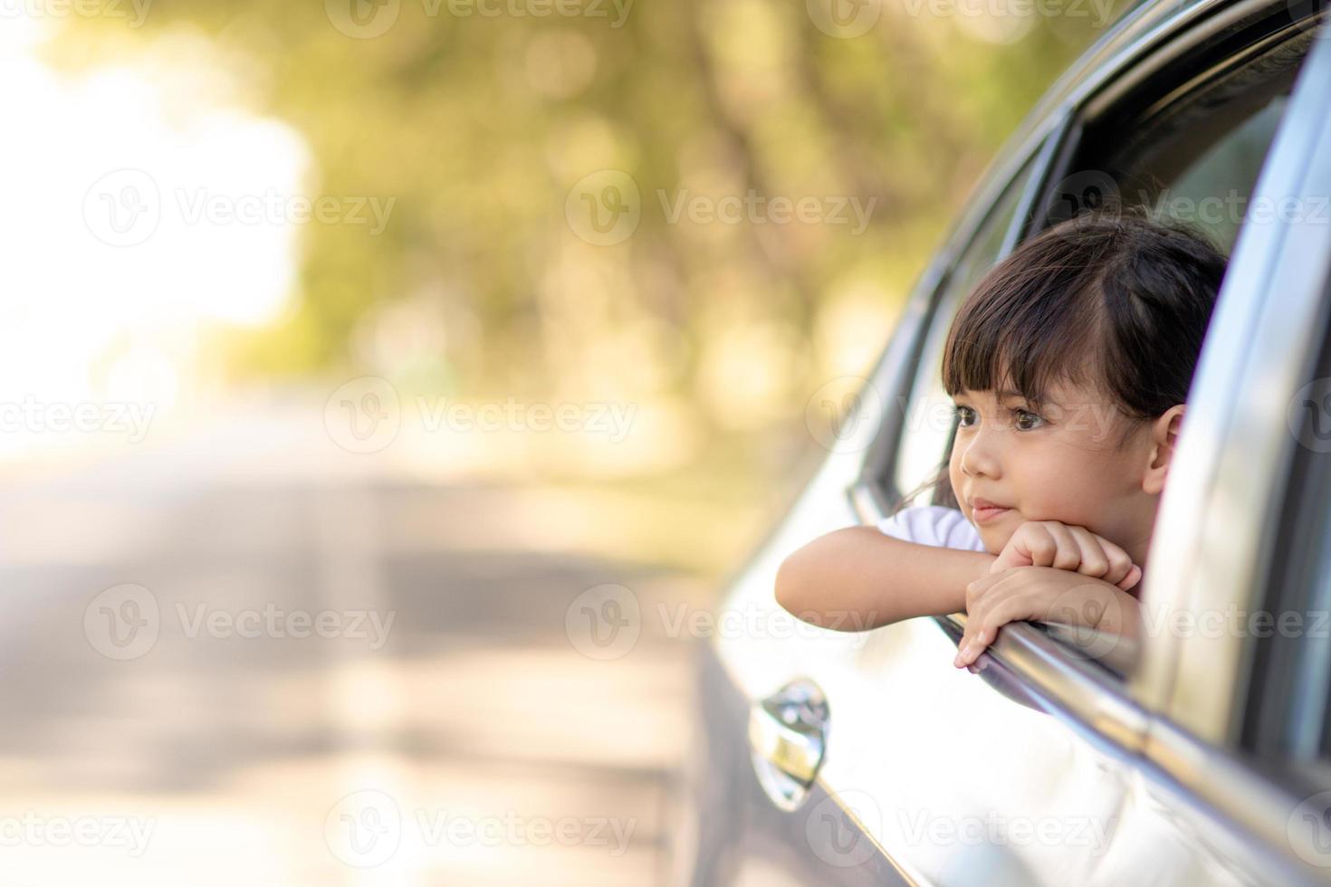 Cute asian little child girl having fun to travel by car and looking out from ar window in cthe countryside photo