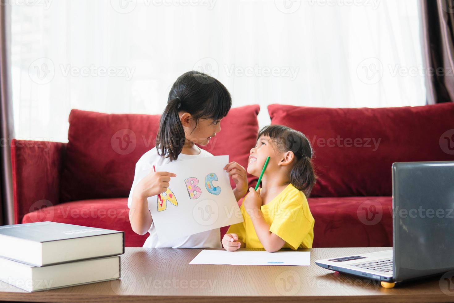 Two asian child girl students study online with teacher by video call together. Siblings are homeschooling with computer laptop during quarantine due to Covid 19 pandemic. photo
