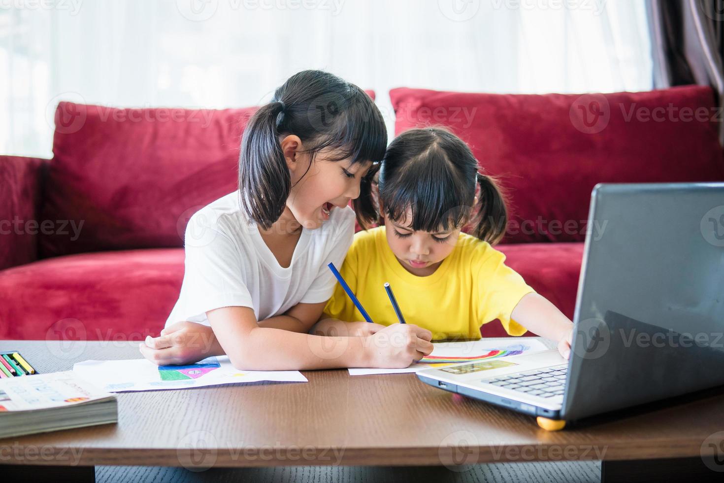 Two asian child girl students study online with teacher by video call together. Siblings are homeschooling with computer laptop during quarantine due to Covid 19 pandemic. photo