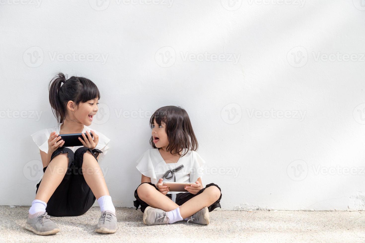 Sibling girls enjoy using smartphones on white background, the Concept of communication technology and people photo