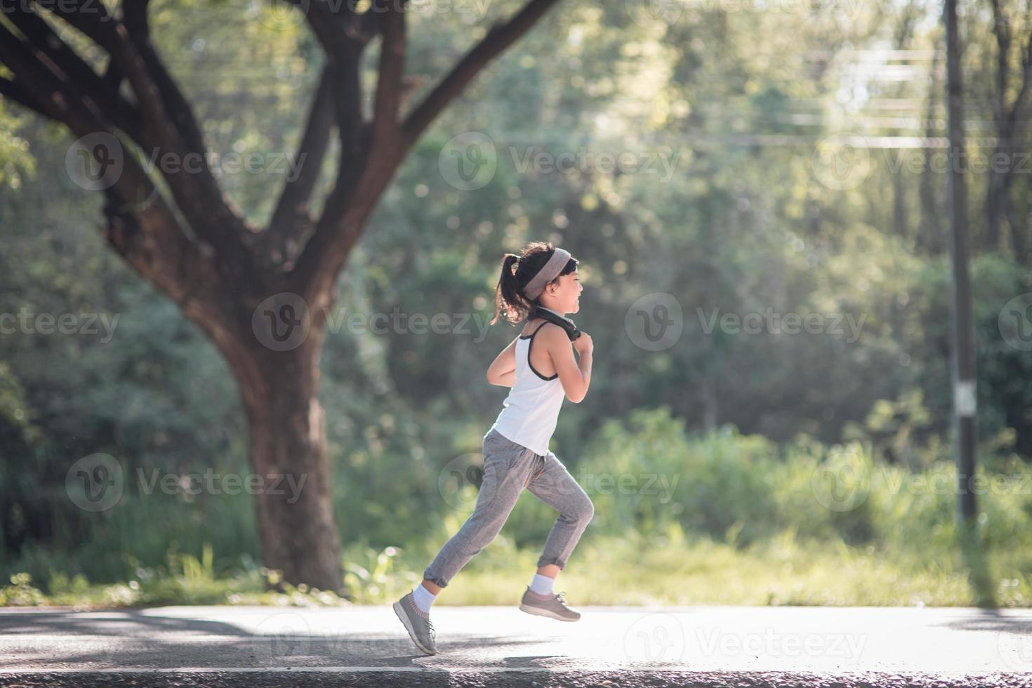 happy child girl running in the park in summer in nature. warm sunlight flare. asian little is running in a park. outdoor sports and fitness, exercise and competition learning for kid development. photo