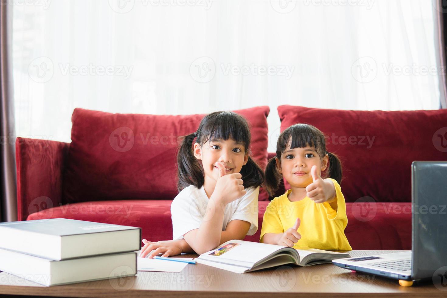 Two asian child girl students study online with teacher by video call together. Siblings are homeschooling with computer laptop during quarantine due to Covid 19 pandemic. photo