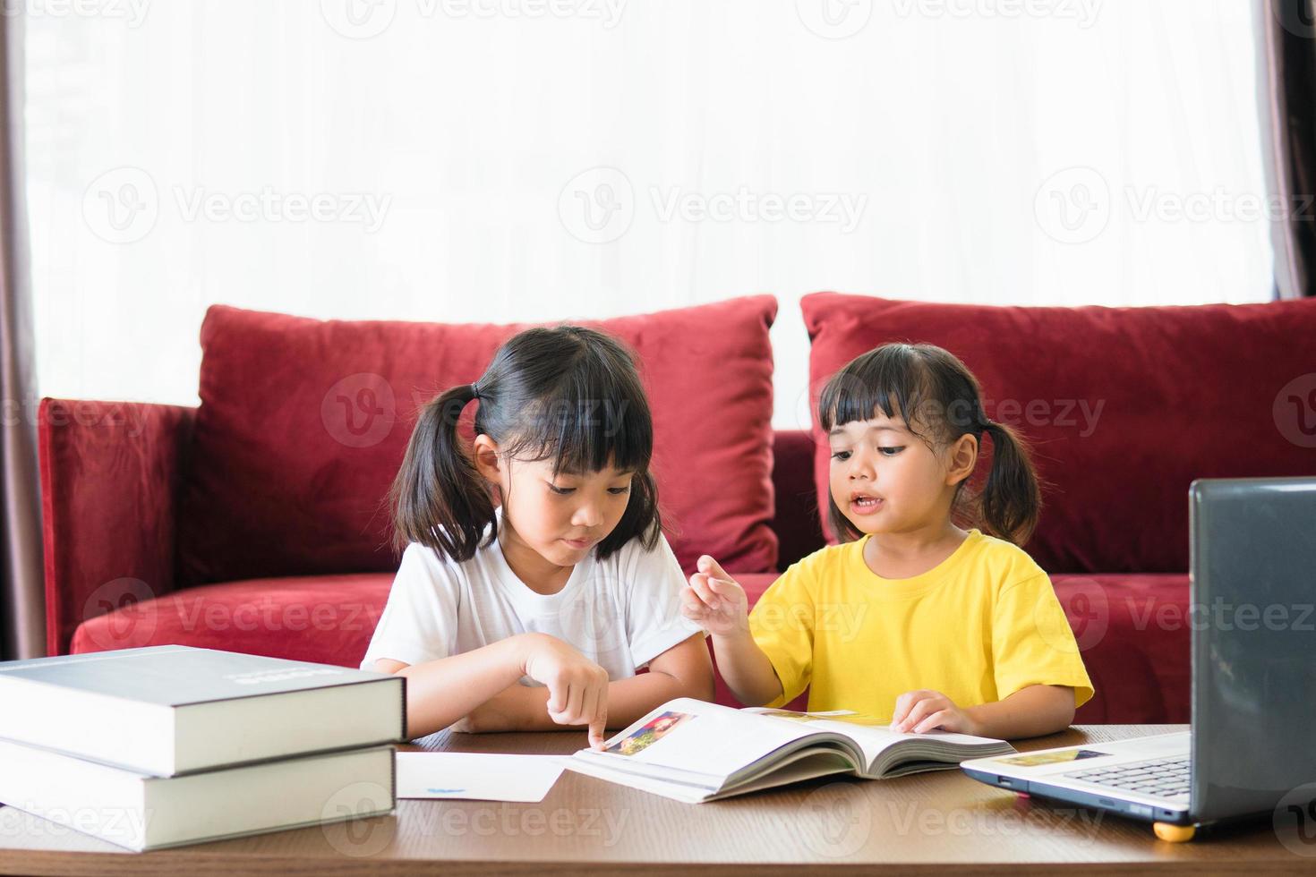 Two asian child girl students study online with teacher by video call together. Siblings are homeschooling with computer laptop during quarantine due to Covid 19 pandemic. photo