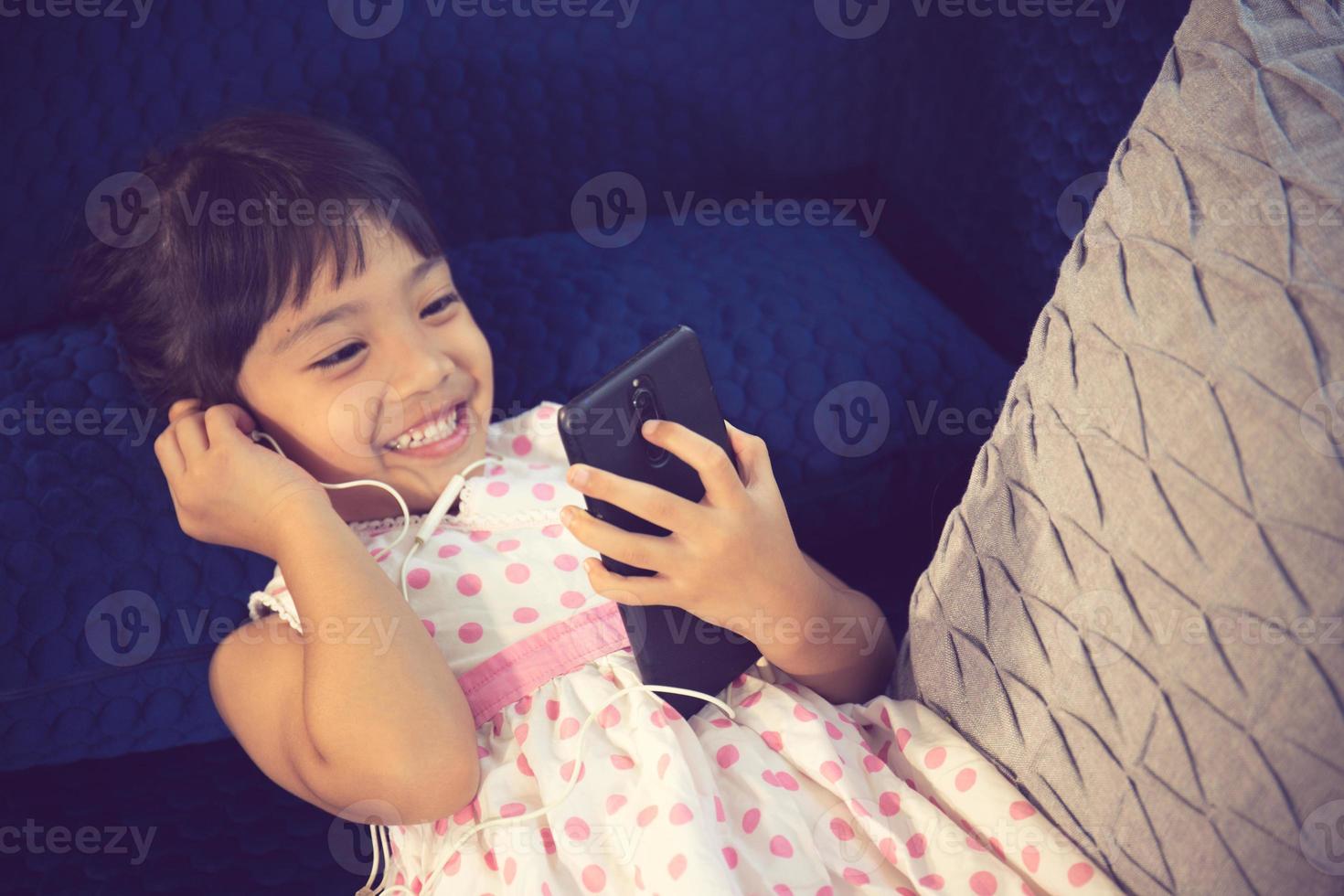Beautiful little girl in headphones using smartphone on a couch photo