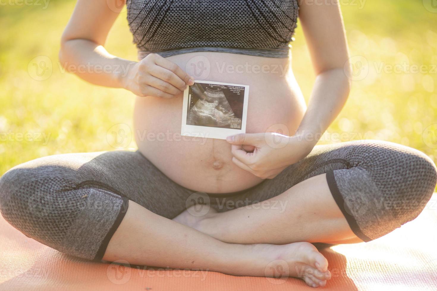Pregnant woman holding ultrasound photo near her pregnant belly