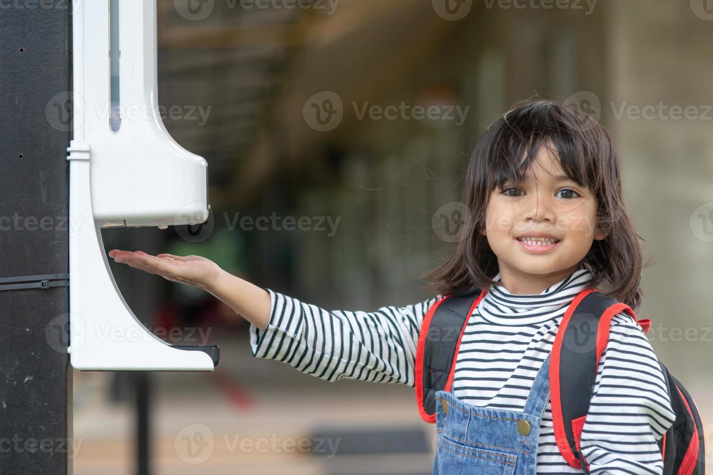 Child girls kid using automatic alcohol gel dispenser spraying on hands sanitizer machine antiseptic disinfectant, new normal life after Coronavirus COVID-19 pandemia. photo