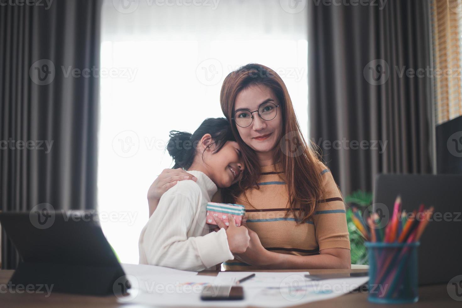 Happy Mother's day. Young woman mom getting congratulations from excited cute little daughter at home, child giving mother gift box while she working on laptop. Family holidays concept photo