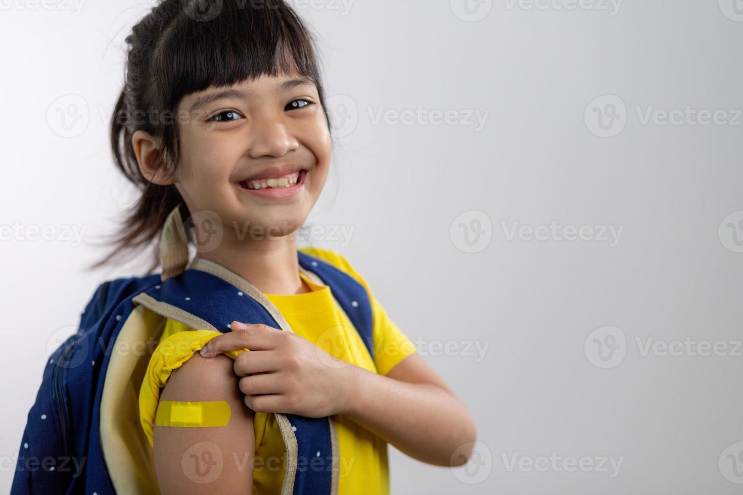 Asian young girl showing her arm with yellow bandage after got vaccinated or inoculation, child immunization, covid delta vaccine concept photo