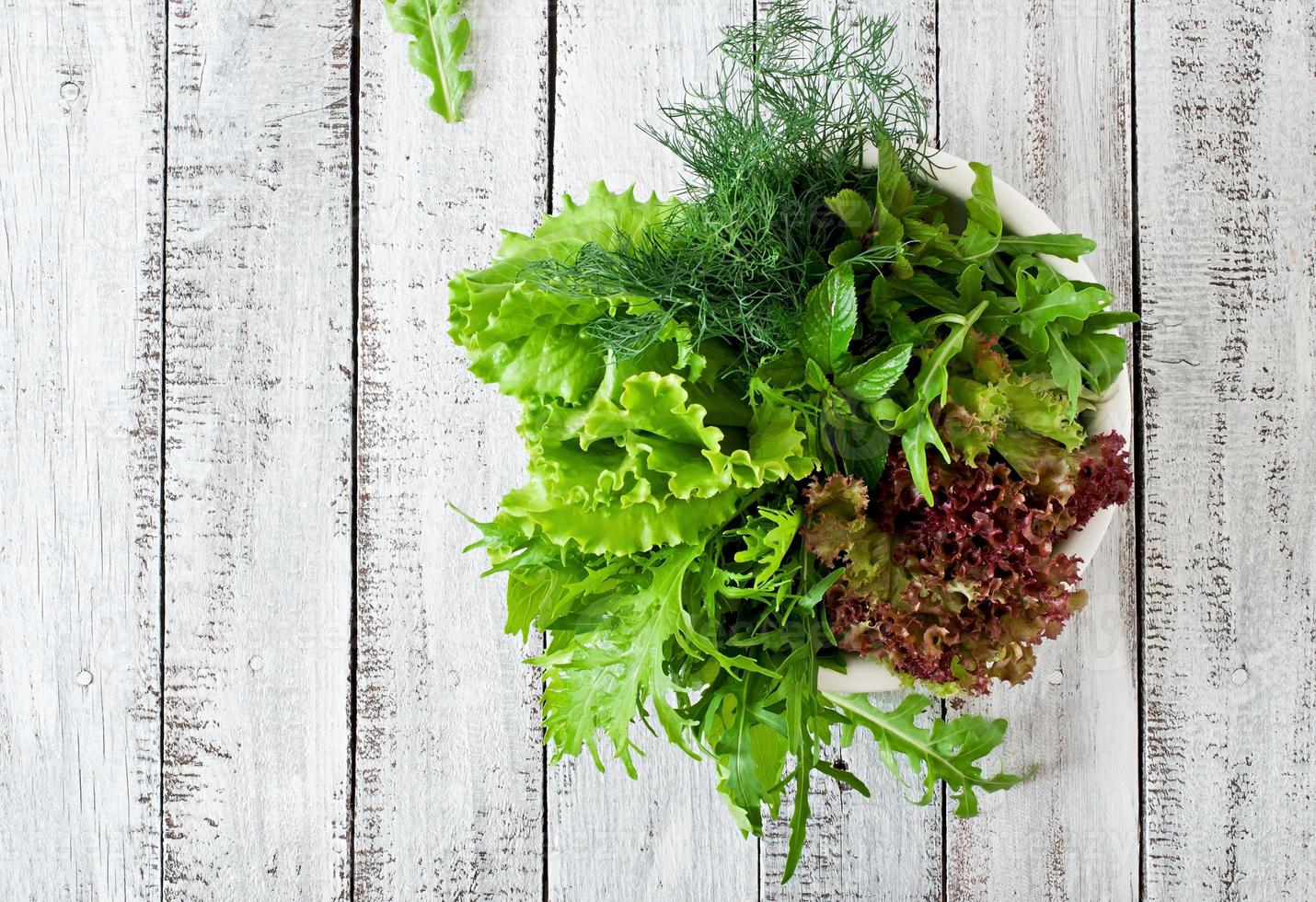 variedad de hierbas orgánicas frescas lechuga, rúcula, eneldo, menta, lechuga roja sobre fondo de madera en estilo rústico foto