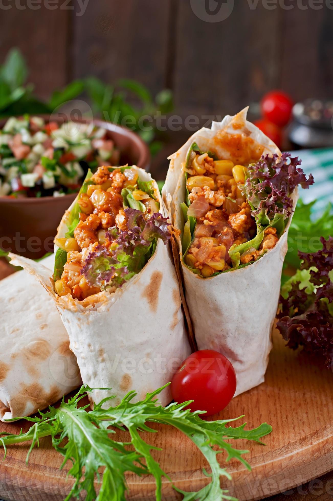 Burritos wraps with minced beef and vegetables on a wooden background