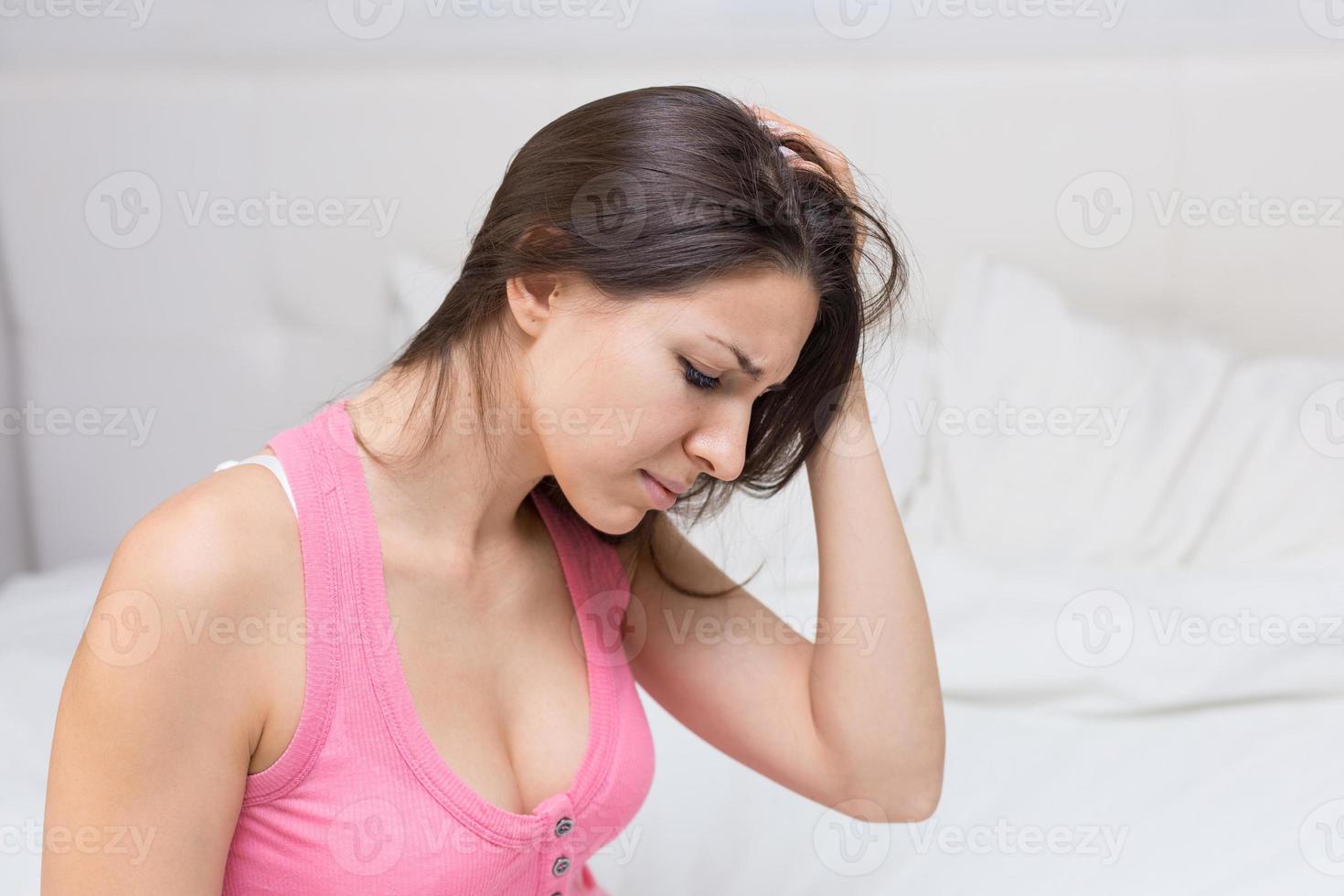 View unhealthy young woman sitting in bed, touching her head, suffering from photo