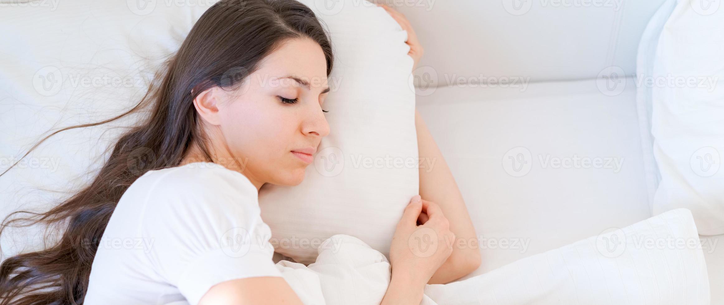 mujer serena y tranquila durmiendo en una cama cómoda acostada sobre una almohada ortopédica blanda foto