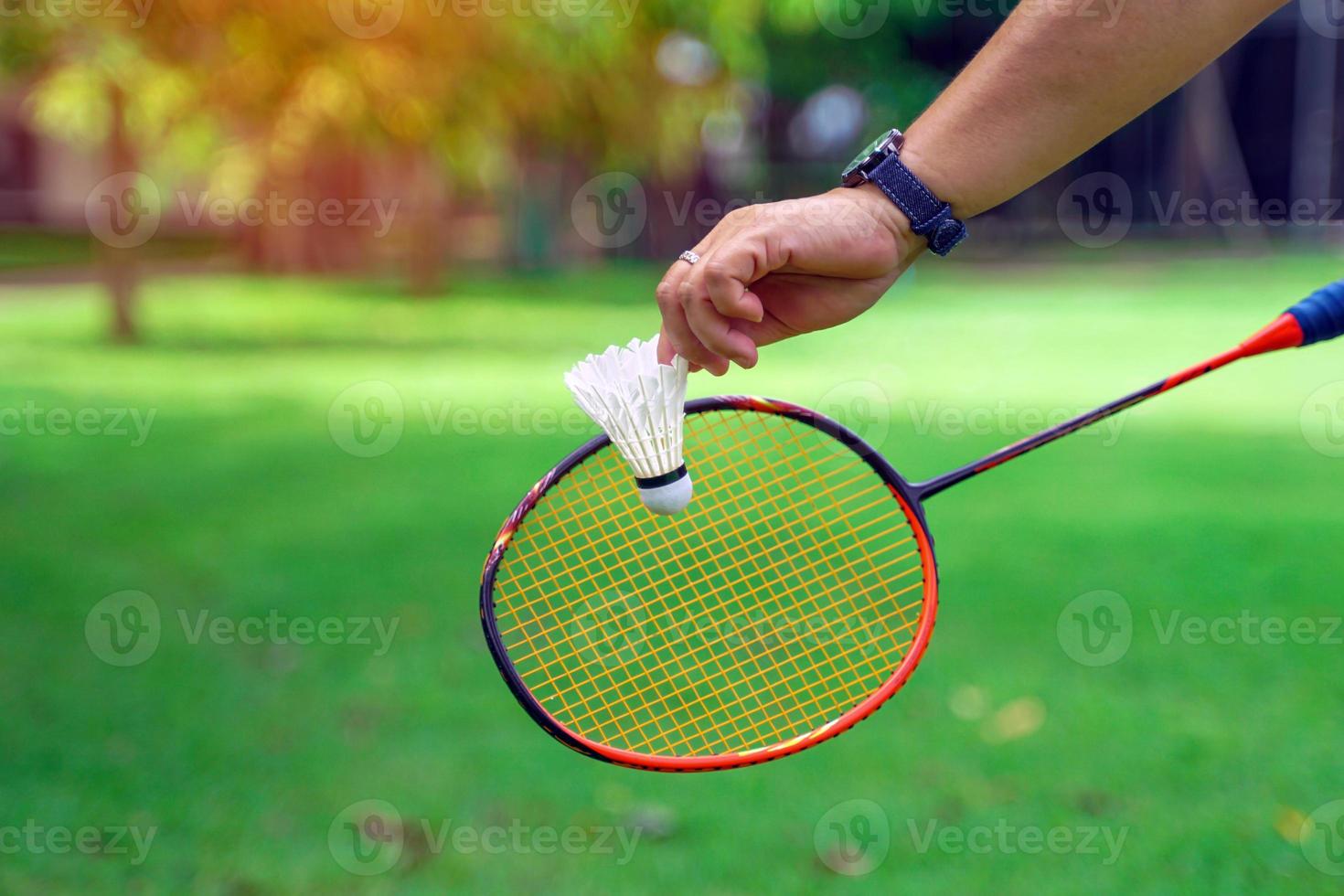 a person holding a shuttlecock in front of a badminton racket, concept for outdoor badminton playing in free times, soft and selective focus. photo