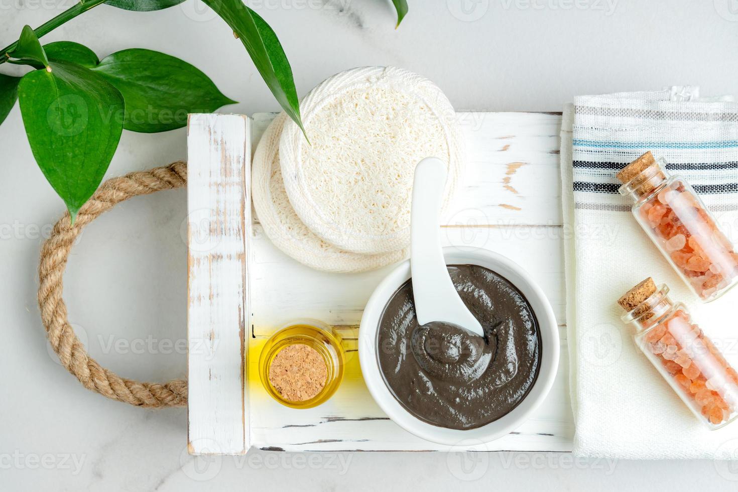 Top view of a bowl with handmade clay mask enriched with natural essential oil on wooden tray. Spa procedures at home. photo