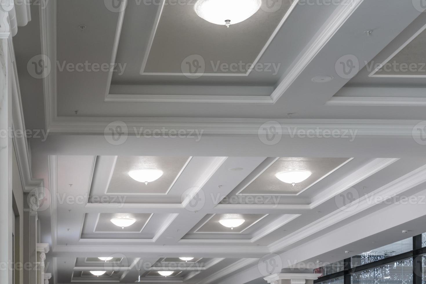 suspended and grid ceiling with halogen spots lamps and drywall construction in empty room in store or house. Stretch ceiling white and complex shape. photo