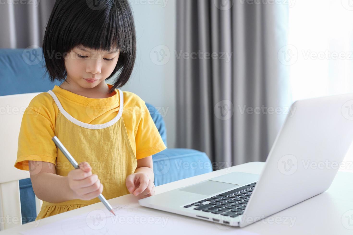 little asian girl student study online using laptop computer at home photo