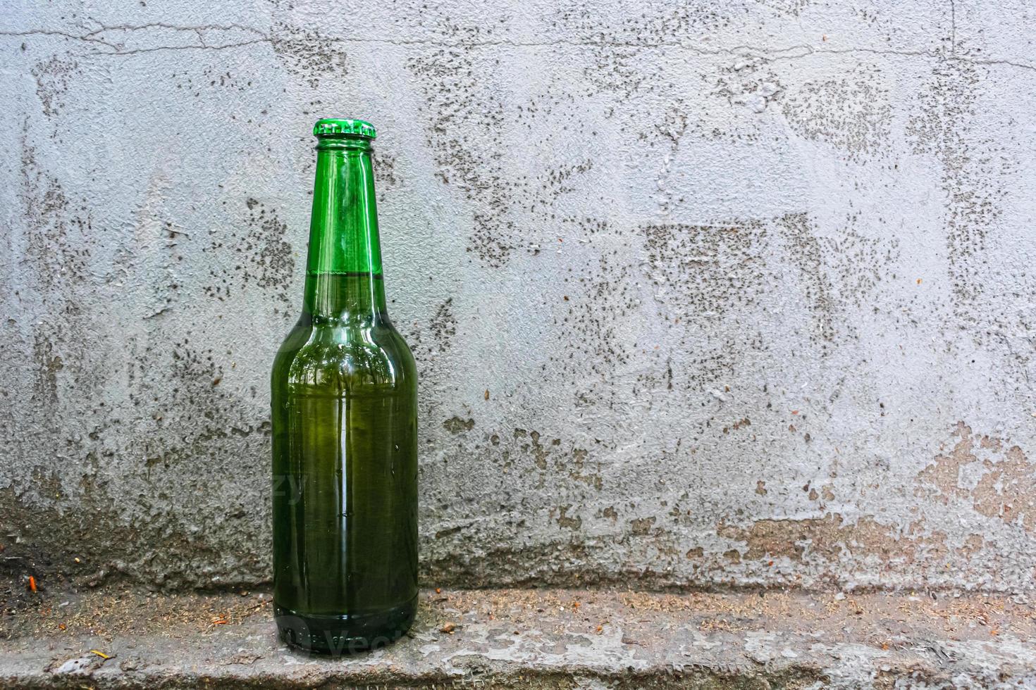 A bottle of beer stands against an old concrete wall photo