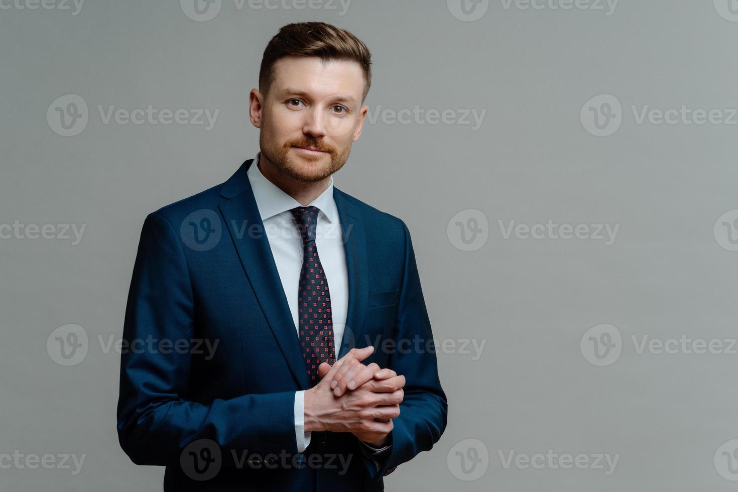 Formal style. Serious bearded male entrepreneur keeps hands together wears formal clothes dressed in office attire poses against grey background with copy space for your promotional content. photo