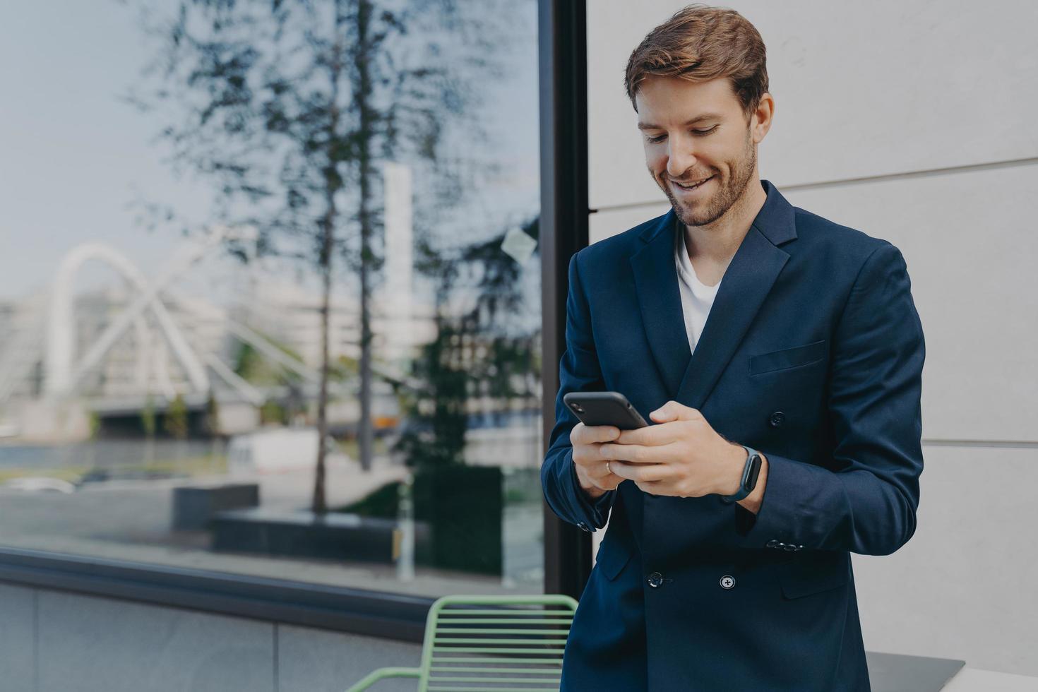 Pleased handsome male CEO or director holds mobile phone waits for call photo