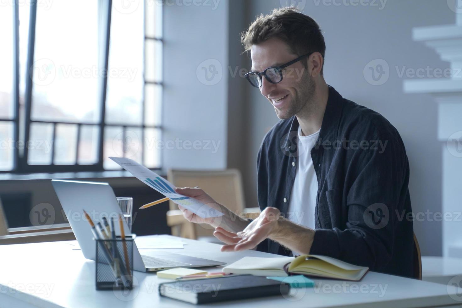 Young German businessman in glasses discussing calculation chart reports with partners online photo