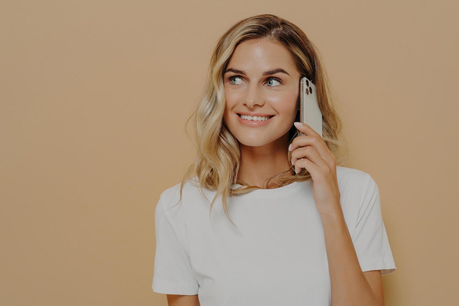 Young blonde smiling woman using cell phone and looking aside, enjoying pleasant conversation with her boyfriend photo