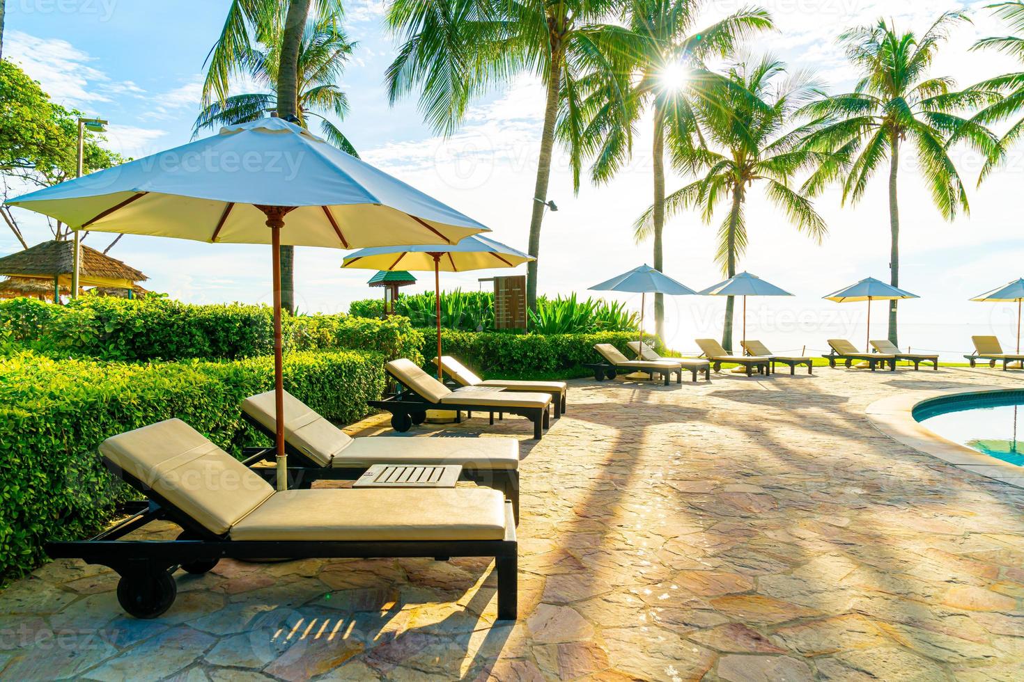 Beautiful luxury umbrella and chair around outdoor swimming pool in hotel and resort with coconut palm tree on blue sky photo