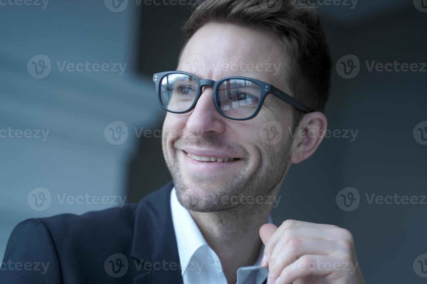 Positive young male entrepreneur in glasses and formal wear looking aside with pleasant smile photo