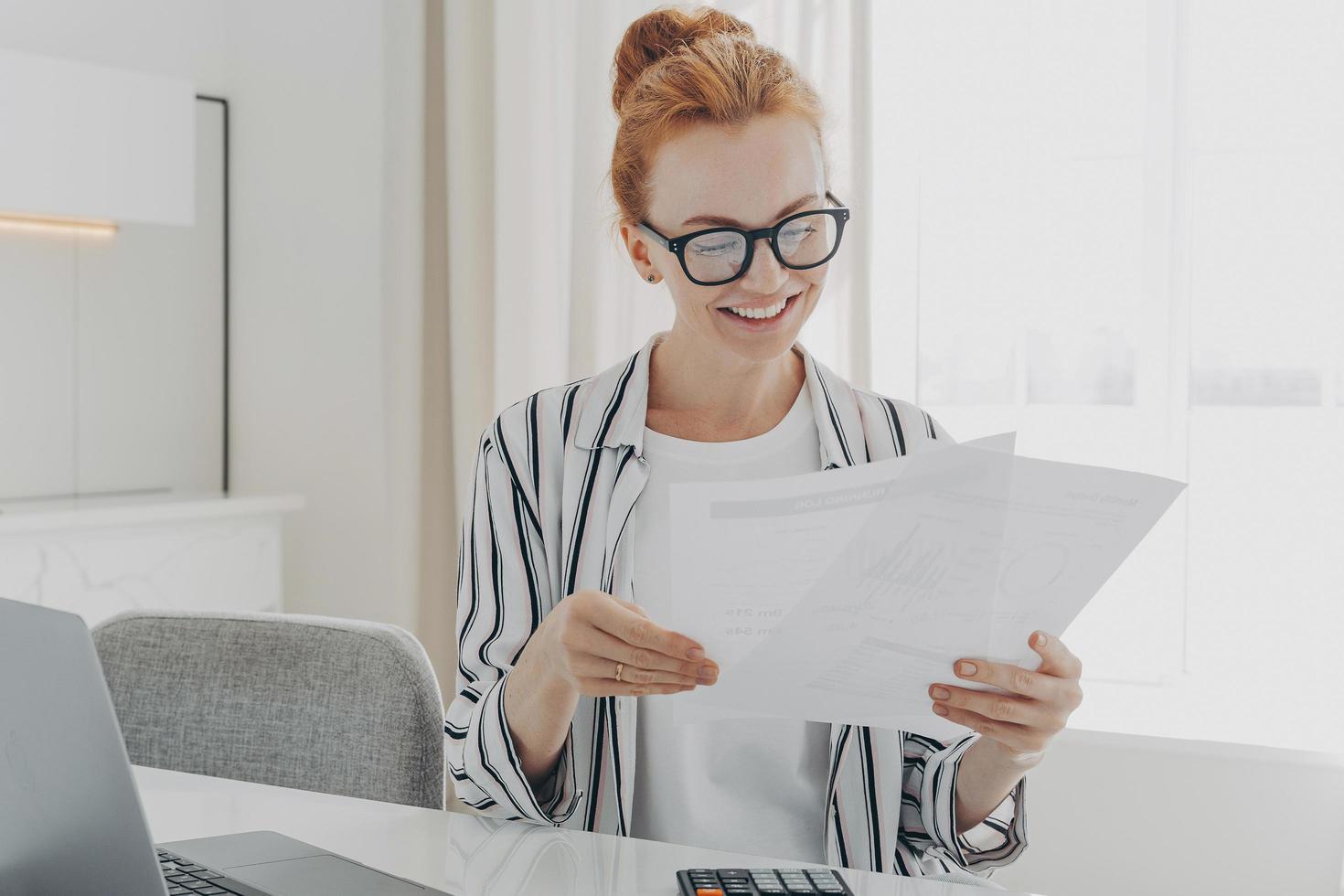 Happy smiling caucasian woman reading good news in financial documents while managing family budget photo