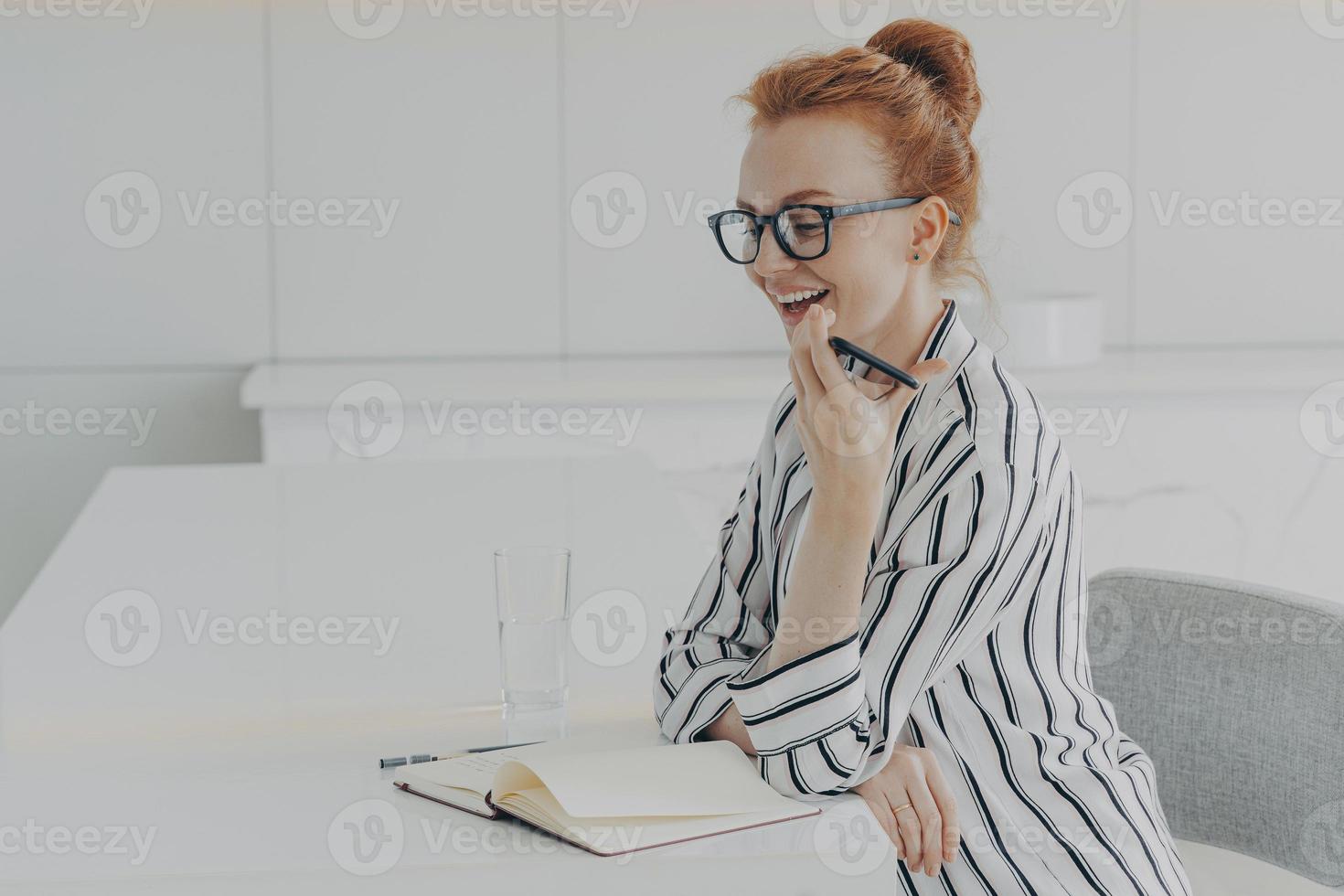 mujer sonriente sosteniendo un móvil y hablando con un asistente virtual de reconocimiento de voz digital en casa foto