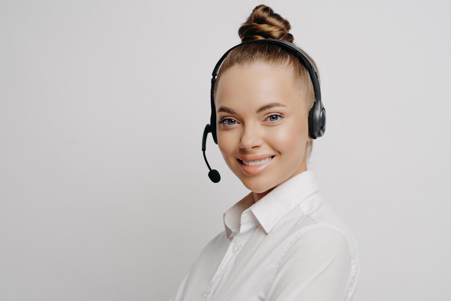 Cheerful woman in white shirt with black headset smiling at camera photo