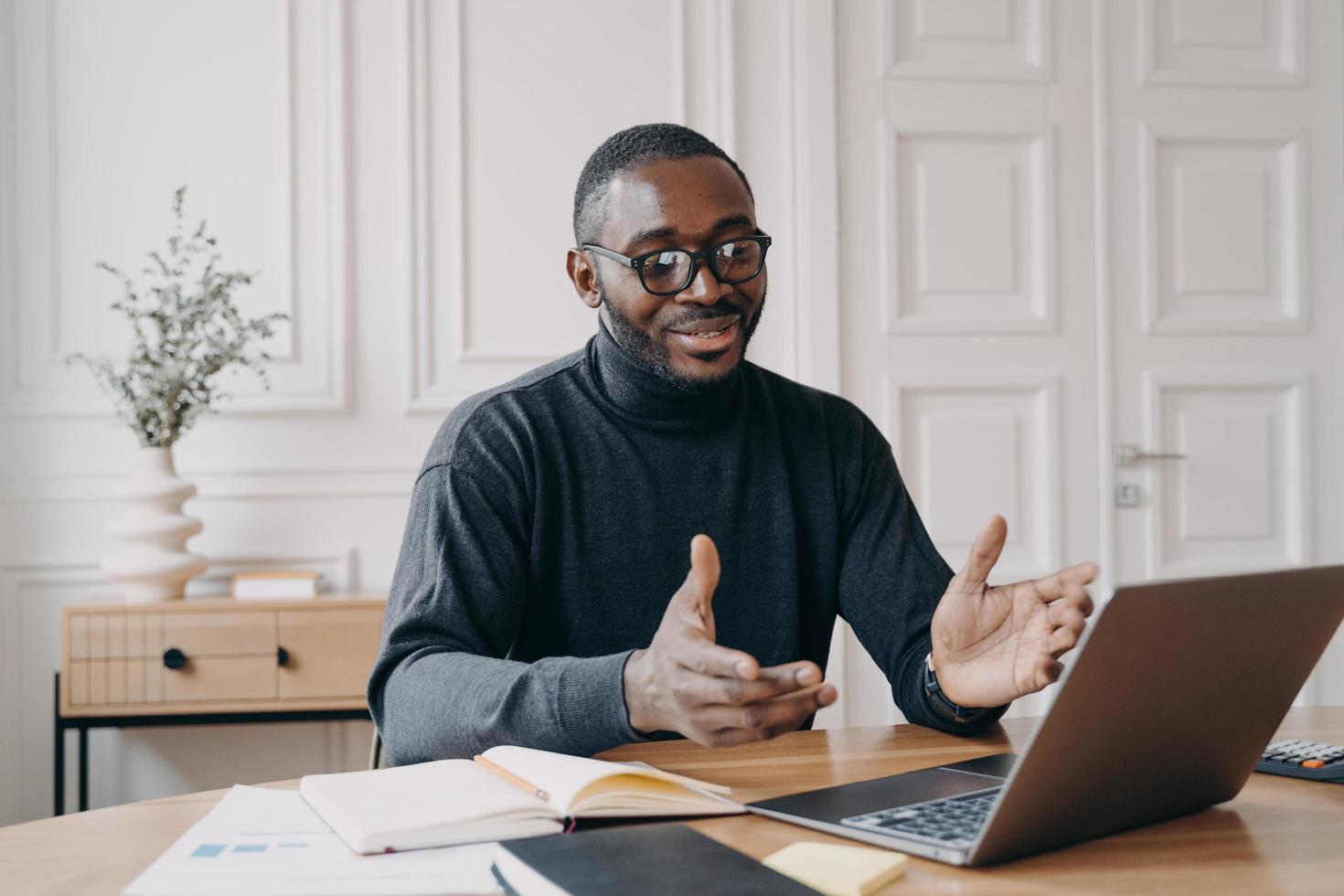 Young smiling african american businessman in glasses enjoying video call on laptop computer photo