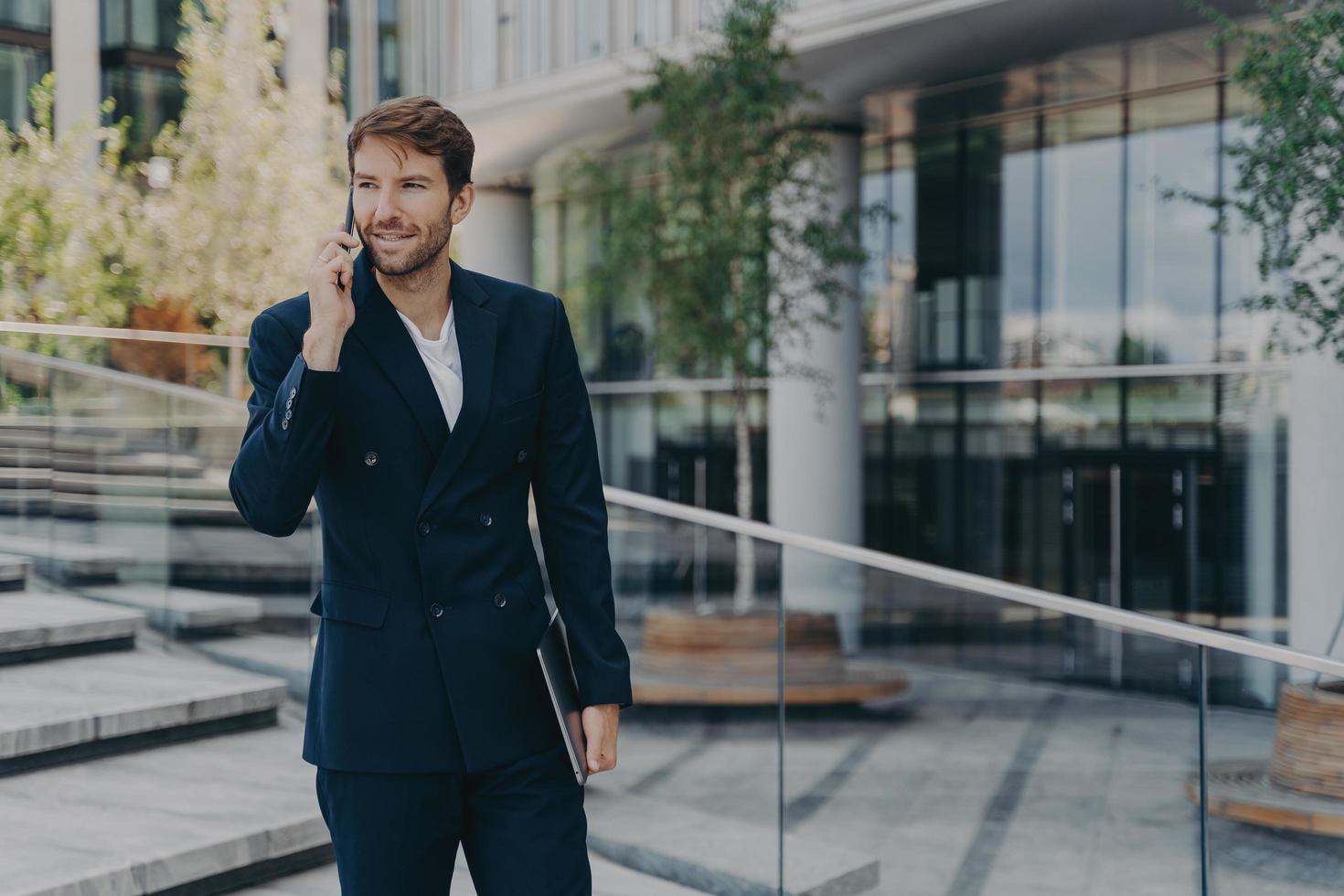 Fashionable unshaven businessman uses modern technologies has telephone conversation holds gadget photo