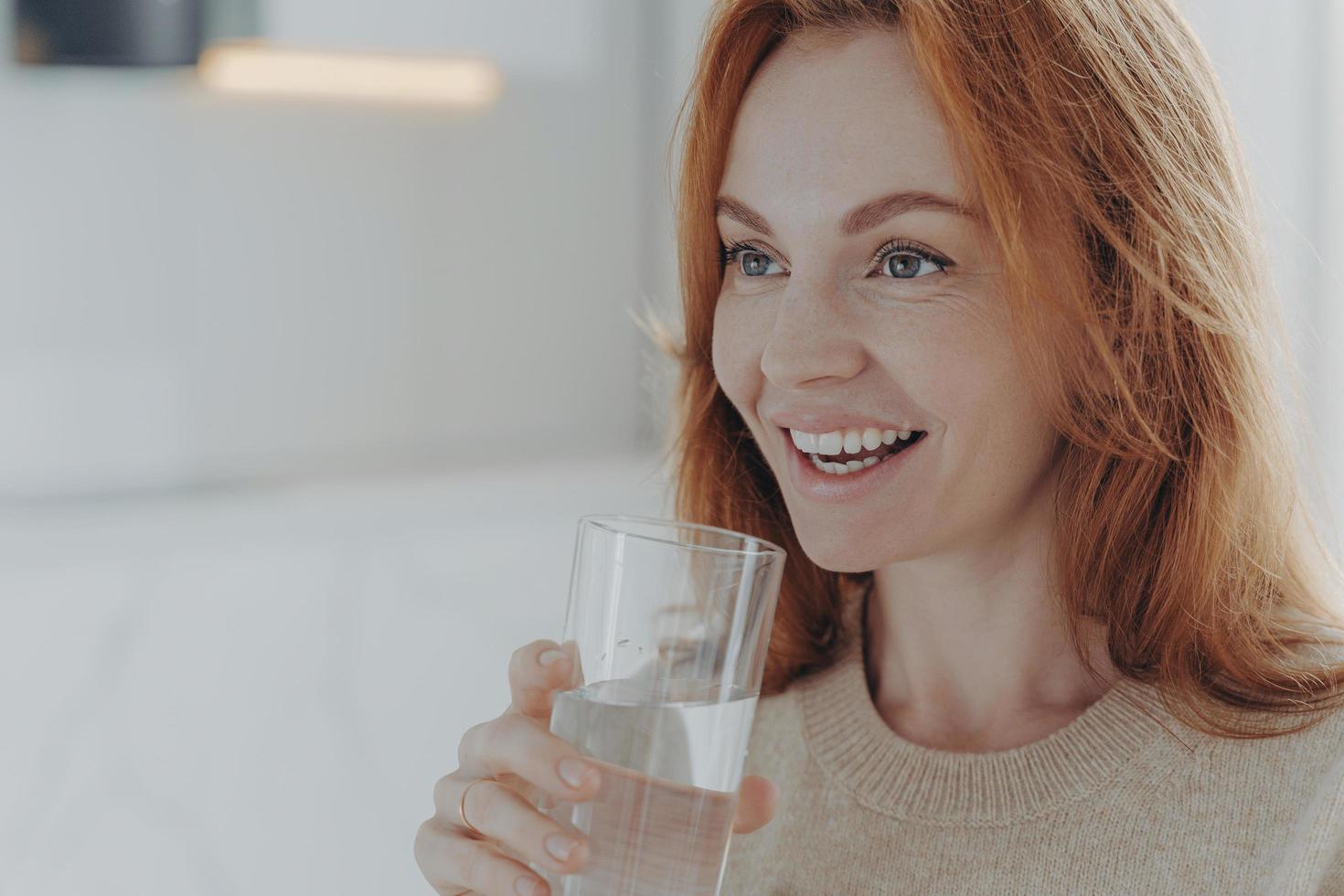 Ginger woman drinks pure water from glass enjoys refreshing drink photo