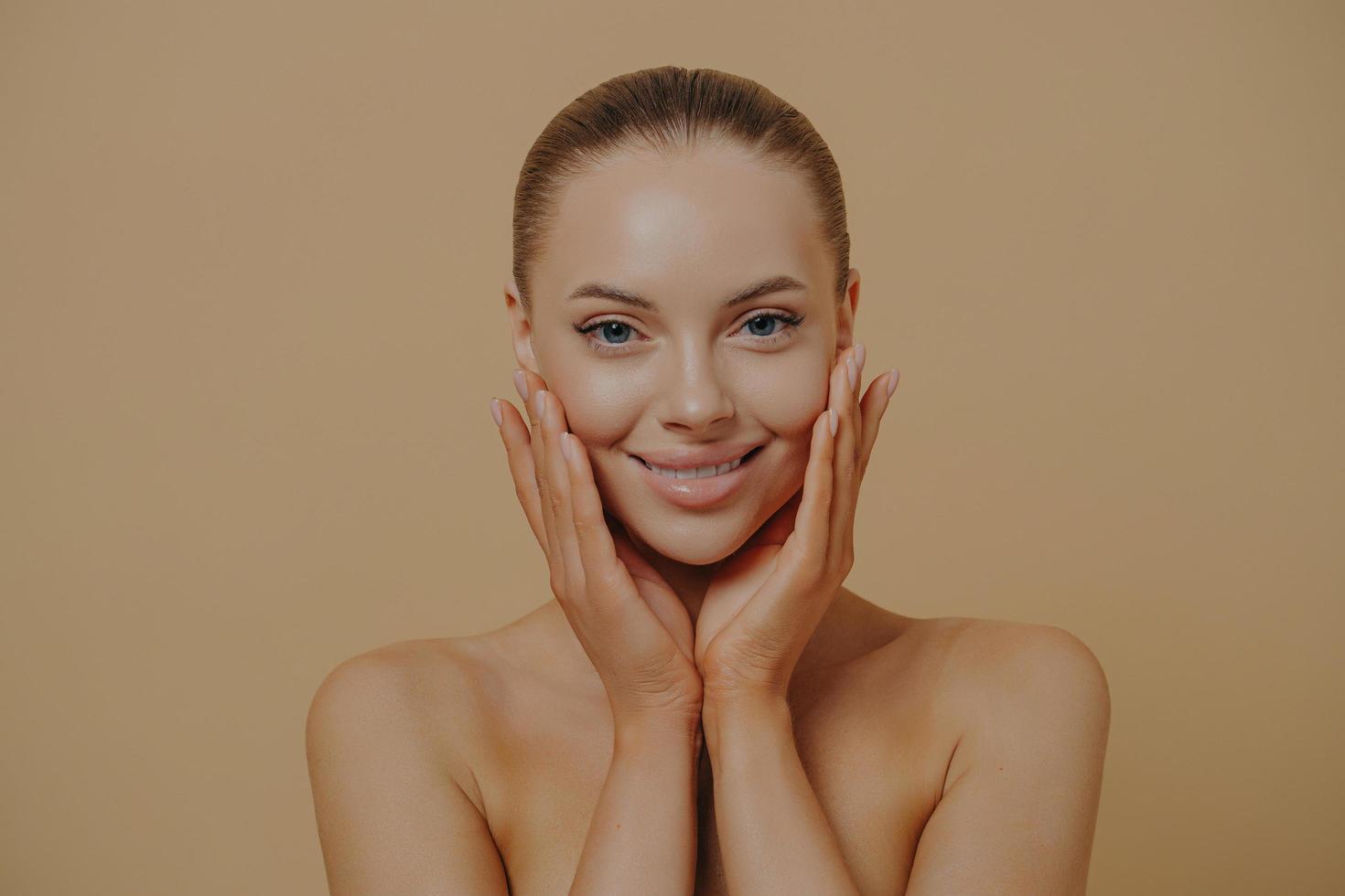 Young beautiful woman with bare shoulders touching cheeks, enjoying her soft and smooth skin photo