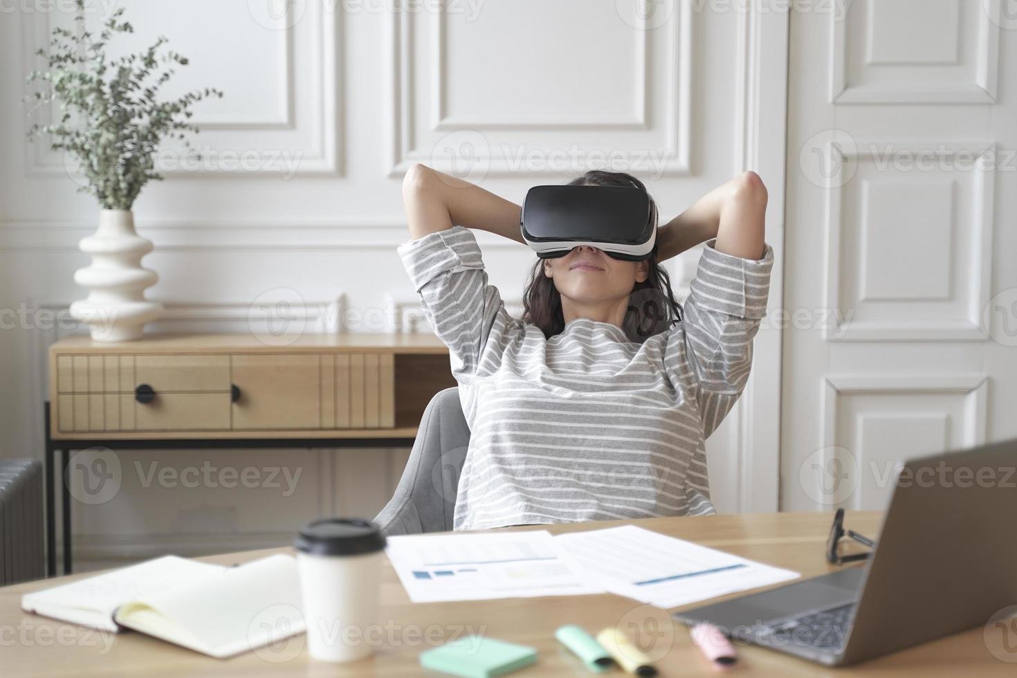 Young glad woman office worker in virtual reality glasses at workplace, relax in VR helmet at work photo