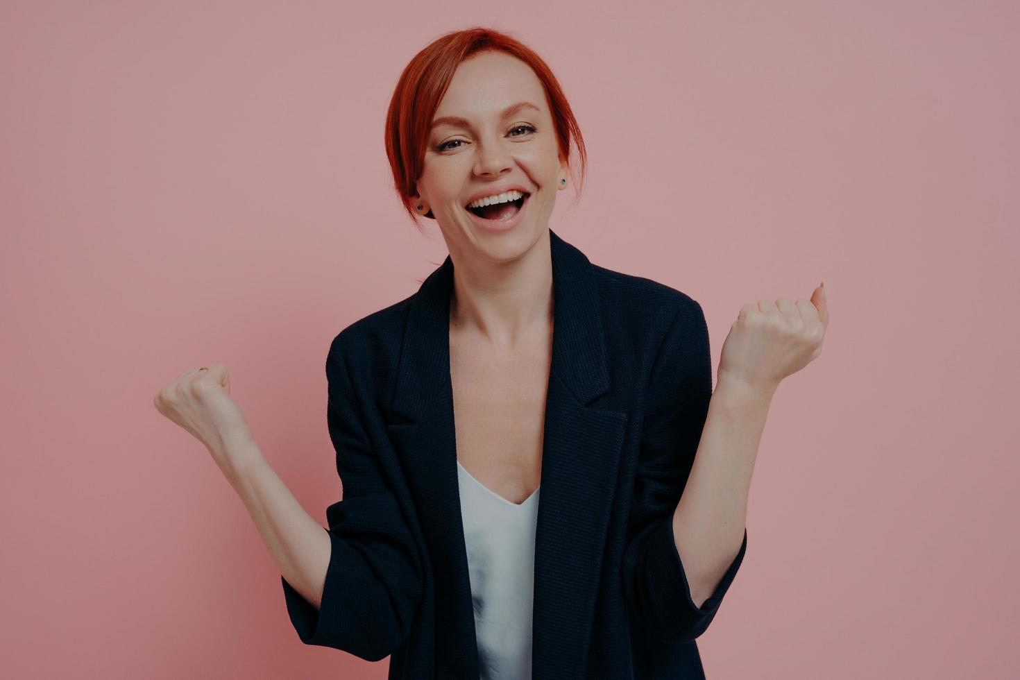 mujer de negocios de jengibre feliz y emocionada aislada de fondo rosa gritando de alegría foto