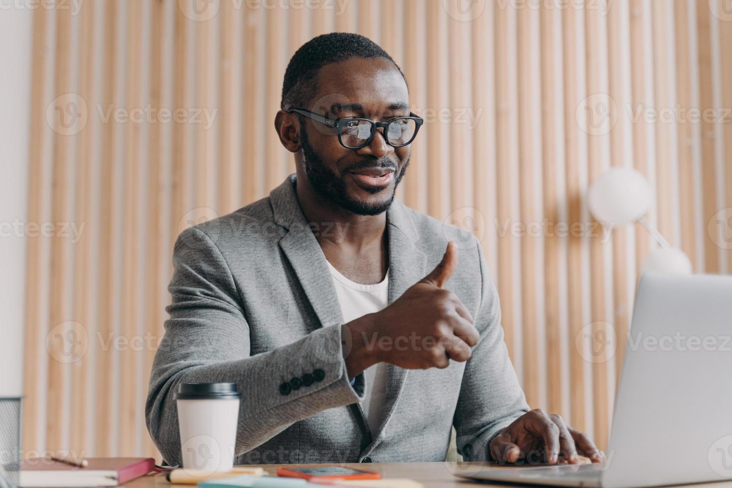 Happy young african american businessman talks online on laptop with client or business partner photo